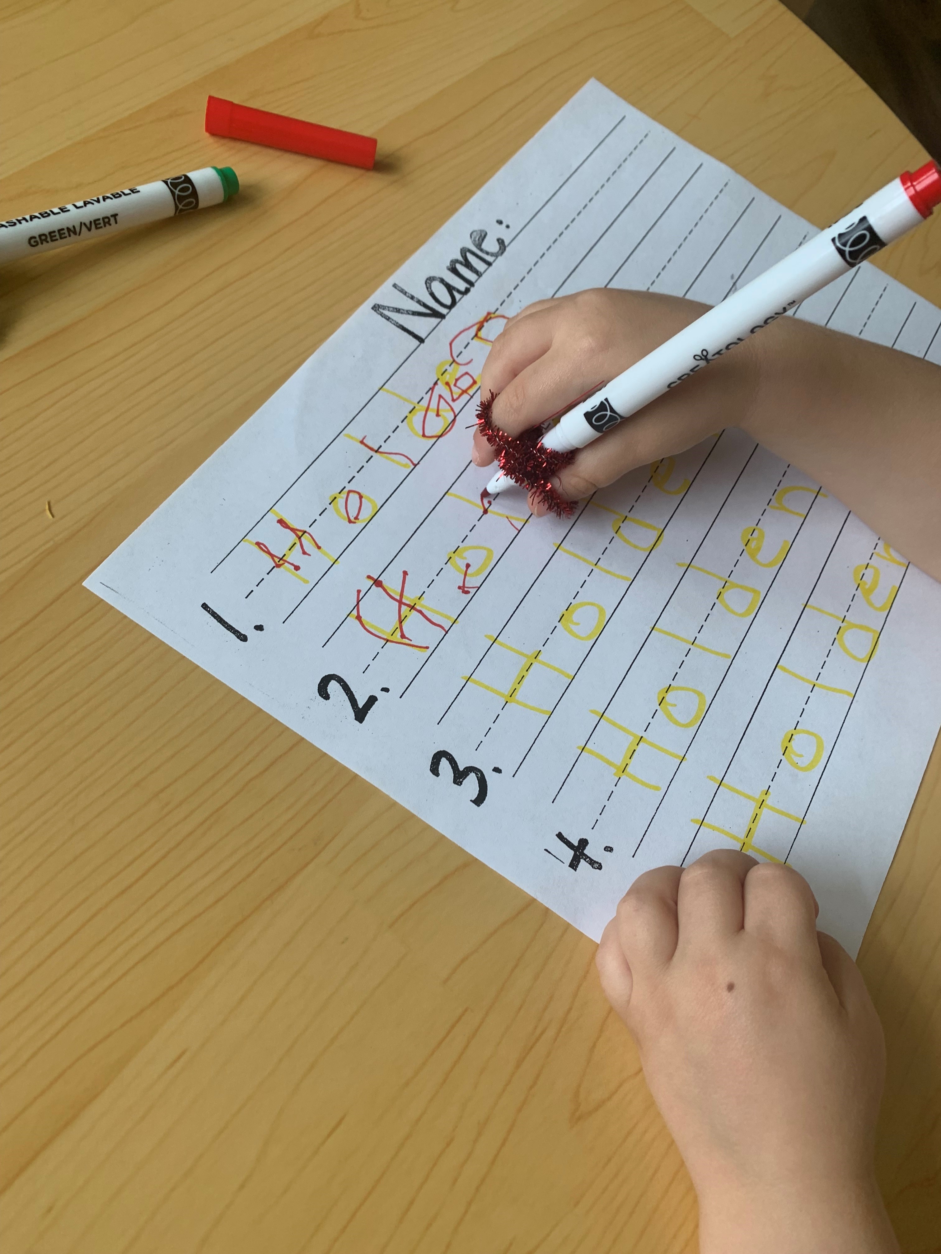 young child uses assistive writing tool to write letters