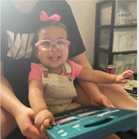 A young girl sits on the floor with her mom and her communication deice